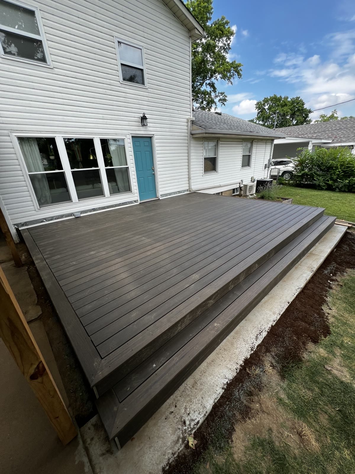 Newly built gray composite deck with steps off a white-sided home